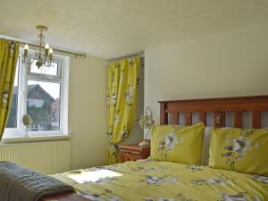 a bedroom with a bed with yellow curtains and a window at Florence Cottage in Pakefield