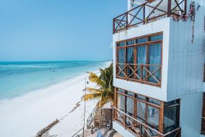 a building on the beach with a palm tree and the ocean at Pili Pili Tropical Island in Jambiani