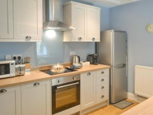 a kitchen with white cabinets and a stainless steel refrigerator at Bluebell Cottage in Alnwick