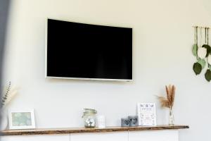 a television on a white wall with a shelf at Reethaus MeerFerien direkt am Wasser in Mellnitz