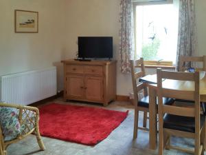 a living room with a television and a table with a red rug at Lismore Cottage in North Ballachulish