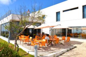 een restaurant met oranje tafels en stoelen en een man bovenop een gebouw bij HI Arrifana Destination Hostel in Aljezur