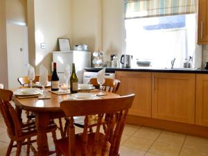 a kitchen with a wooden table with wine bottles and chairs at Kirsty Cottage in Moffat