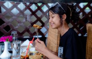 a woman sitting at a table eating food with a fork at Hotel Quick Twenty and Riverside Pvt Ltd in Amlekhganj