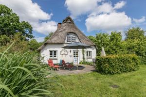 a thatched cottage with two chairs and an umbrella at Ferienhaus Kleiner Knopp in Glücksburg