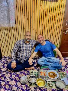 two men are sitting on a blanket with food at Sea Green Guest House in Srinagar