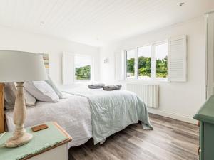 a white bedroom with a bed and two windows at Holiday Home Cobble Cottage by Interhome in Lerryn
