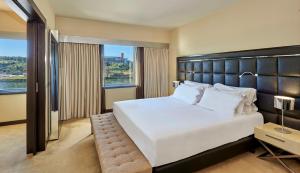 a bedroom with a large white bed with a large window at NH Coimbra Dona Ines in Coimbra
