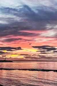 a sunset over the ocean with a lighthouse in the distance at Holiday Home Waters Edge by Interhome in Lossiemouth