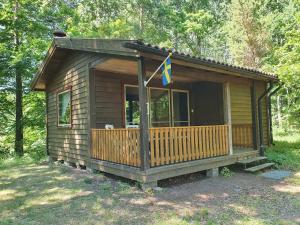 a small cabin with a porch and a flag on it at Cozy cottage with its own beach plot and rowing boat in Linneryd