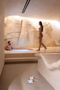 费拉Aressana Spa Hotel & Suites - Small Luxury Hotels of the World的一名男子和一名女子在浴缸前行走