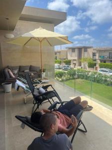zwei Jungen liegen auf Stühlen auf einer Terrasse mit einem Sonnenschirm in der Unterkunft Swan lake magical chalet! North coast in Zāwiyat al ‘Awwāmah