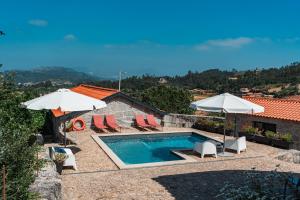 a swimming pool with chairs and umbrellas and a house at Villa Seara - Casas da Vinha in Celorico de Basto