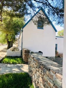 een wit gebouw met een stenen muur ervoor bij Sister Alice in Nieu-Bethesda