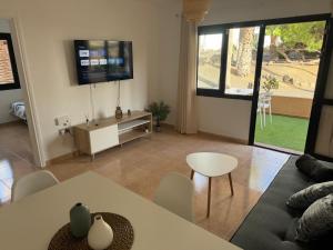 Una sala de estar con un sofá y un televisor en la pared. en Casa Olivia Oasis Duna, en Corralejo