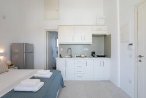 a white kitchen with white cabinets and towels on a bed at Ventus Studios in Ano Mera