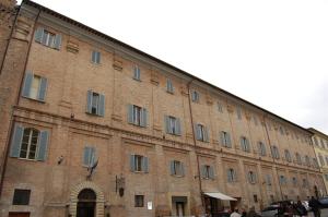 un grand bâtiment en briques avec des personnes debout devant lui dans l'établissement Guest House Domus Urbino, à Urbino