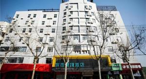 ein hohes weißes Gebäude mit Bäumen davor in der Unterkunft City Comfort Inn Fuyang Hongqi Middle School Erlijing Night Market in Fuyang