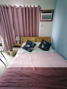 a bed with two pillows in a bedroom with pink curtains at Coastal Stay at Oceancrest in Cebu City +14 photos