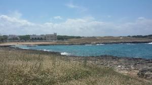 a beach with blue water and a house in the background at Hotel Corallo in Torre Santa Sabina