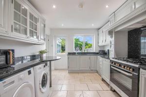 a kitchen with white cabinets and a washer and dryer at The Roost Group - Brands Hatch 6 Bedroom Home in Fawkham