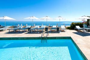 a swimming pool with tables and chairs and the ocean at Hôtel Pineto in Biguglia