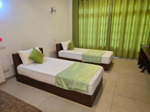 two beds in a room with green curtains at Hotel Serugahawatta in Wellawaya