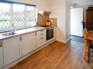 a kitchen with white cabinets and a wooden floor at Bournstream Cottage in Withycombe