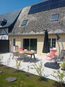 a patio with a table and an umbrella and a house at Le gîte de notre histoire in Épégard