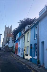 eine Reihe bunter Häuser in einer Straße mit einer Kirche in der Unterkunft "FISHERMAN'S" Seconds from the Harbour & town centre with unlimited free parking nearby in Brixham