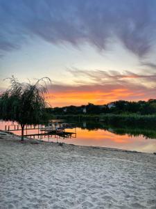 Una puesta de sol en una playa con mesas de picnic y un lago. en Кемпінг, намети, en Surskoye