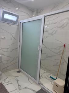 La salle de bains est pourvue de murs en marbre et d'une porte de douche en verre. dans l'établissement AL MIDIAF STYLISH VILLA &Garage, à Mostaganem