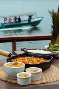 a table with two pans of food and a boat at Pousada Pôr Do Sol - Ilha do Mel - Nova Brasília in Paranaguá