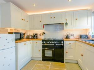 a kitchen with white cabinets and a black stove top oven at Whibberley Cottage in Ashford +18 photos