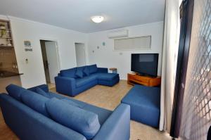 a living room with blue couches and a flat screen tv at Villa Palazzo 3 - Kalbarri, WA in Kalbarri