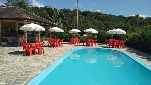 a swimming pool with red chairs and umbrellas at Recanto Da Mata in Morretes