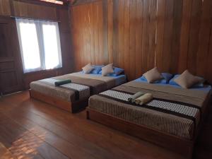 two beds in a room with wooden walls and a window at JN Cottage dan Camping Ground in Karimunjawa