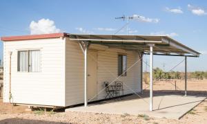 une petite maison blanche avec un toit sur un terrain en terre dans l'établissement Birdsville Tourist Park, à Birdsville