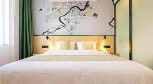 a bedroom with a large white bed with green curtains at Vatica Hotel Haikou Jinniuling Park Haizhiyuan in Haikou