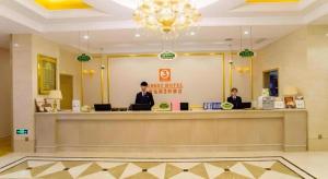 zwei Personen sitzen an einem Tresen in einer Hotellobby in der Unterkunft Vienna 3 Best Shanghai Baoshan Fengxiang Road in Chenjiahang