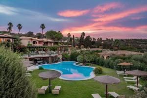 a resort with a swimming pool and lawn with umbrellas at Hotel Mariposas in Villasimius