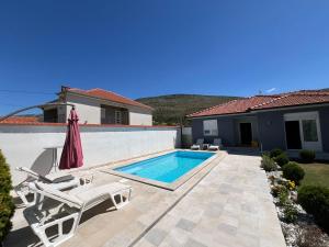 a swimming pool in a yard with two chairs and an umbrella at Vila Dolce Vita Mostar in Mostar