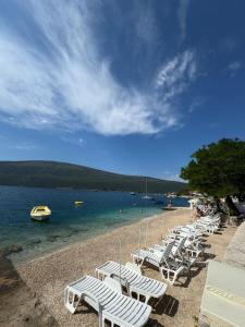 a group of white lounge chairs on a beach at Djenovici Herceg Novi in Ðenovići