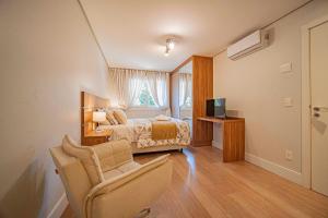 a bedroom with a bed and a chair and a television at L'Adresse Réserve 150m R Coberta by Achei Gramado in Gramado