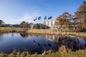 three flags flying over a pond in front of a building at Appartement De Noordkaap in Hollum