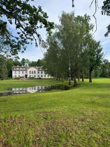 a large white house with trees and a pond at Meirānu muiža in Meirāni