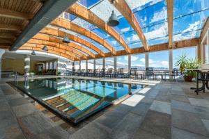 una gran piscina cubierta con techo de cristal, mesas y sillas en Hotel Alpenfrieden, en Maranza