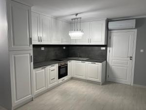 a white kitchen with white cabinets and a chandelier at ЛУКСОЗНИ АПАРТАМЕНТИ ДАРИС-free parking in Kazanlŭk