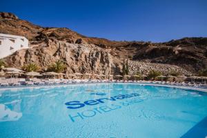 a large swimming pool with chairs and a mountain at Servatur Terrazamar Sun Suite in Puerto Rico de Gran Canaria