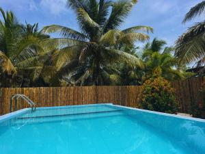 a swimming pool in front of a fence with palm trees at The Shenu Lake House in Dandugama +31 photos